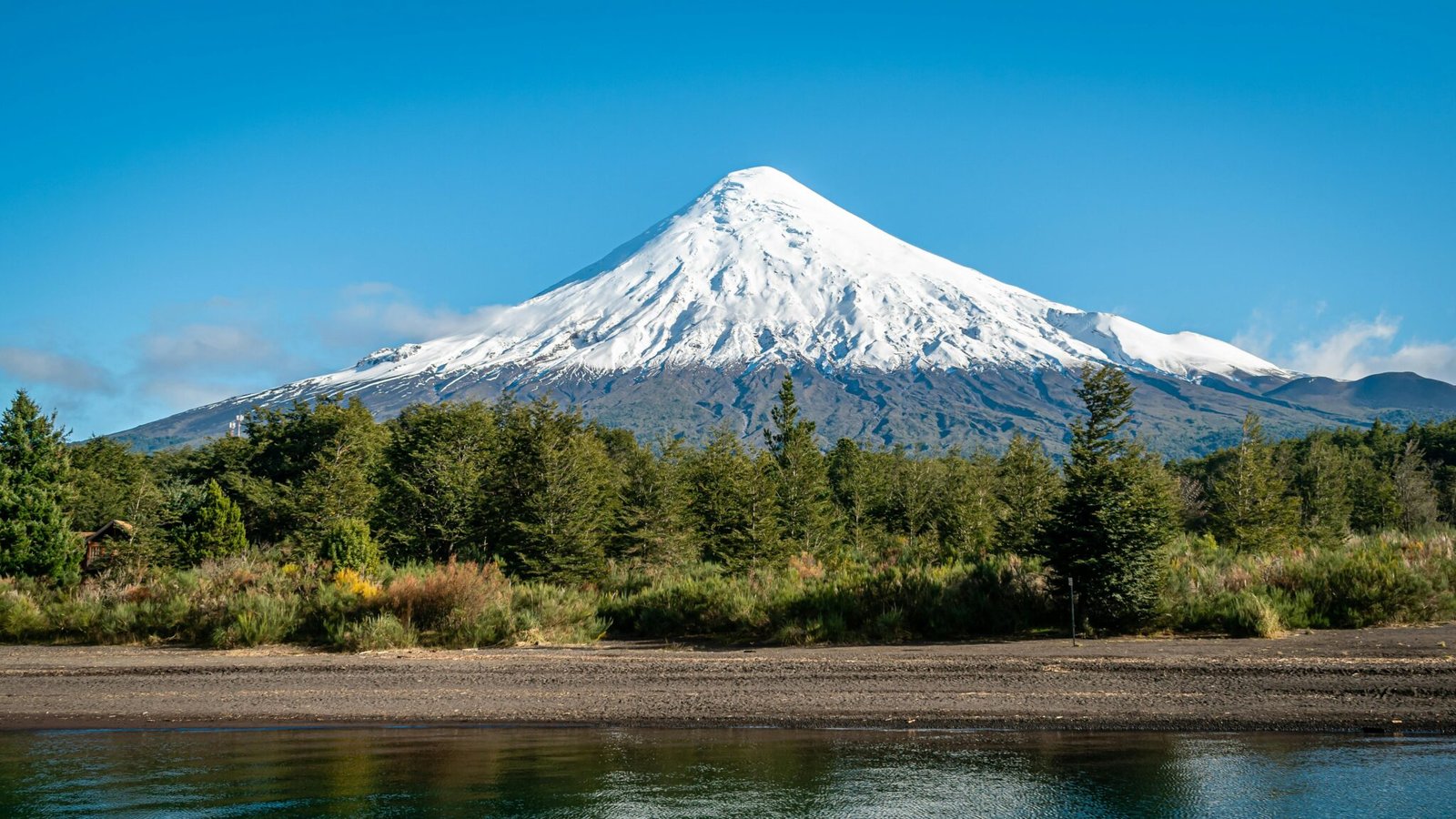 Scenic view of the snow-capped Osorno Volcano in Chile, surrounded by lush forests and blue skies.